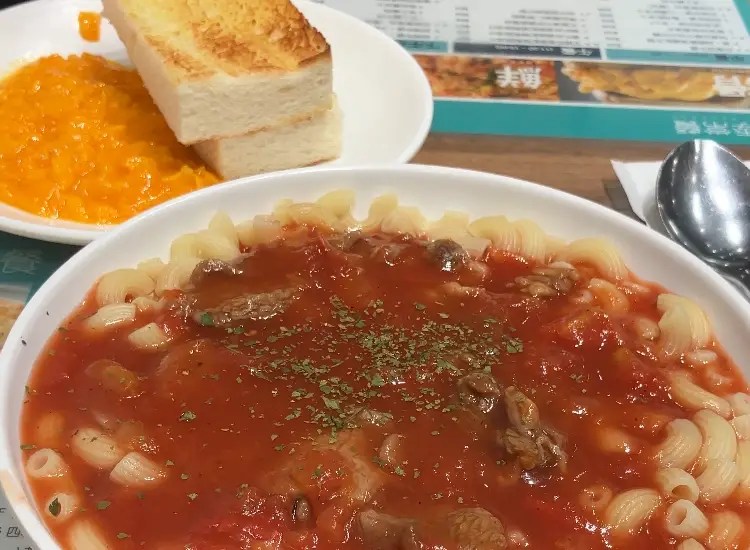 一碗番茄醬義大利麵，上面撒有香料，旁邊有兩片烤土司和一碗橘色甜點。