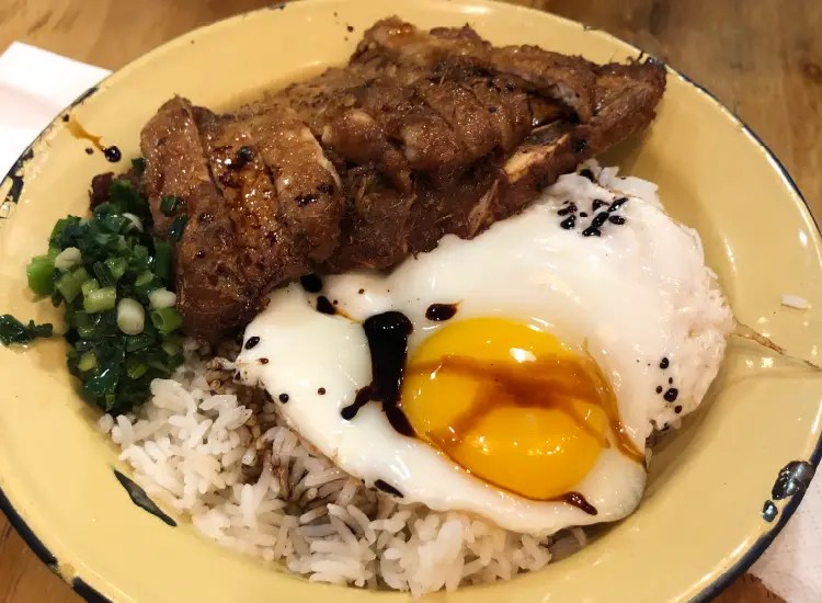 一碗米飯，上面放有煎蛋和醬燒肉，旁邊有切碎的青蔥。